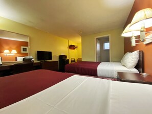 A hotel room with two beds, a desk, a television, and a lamp.