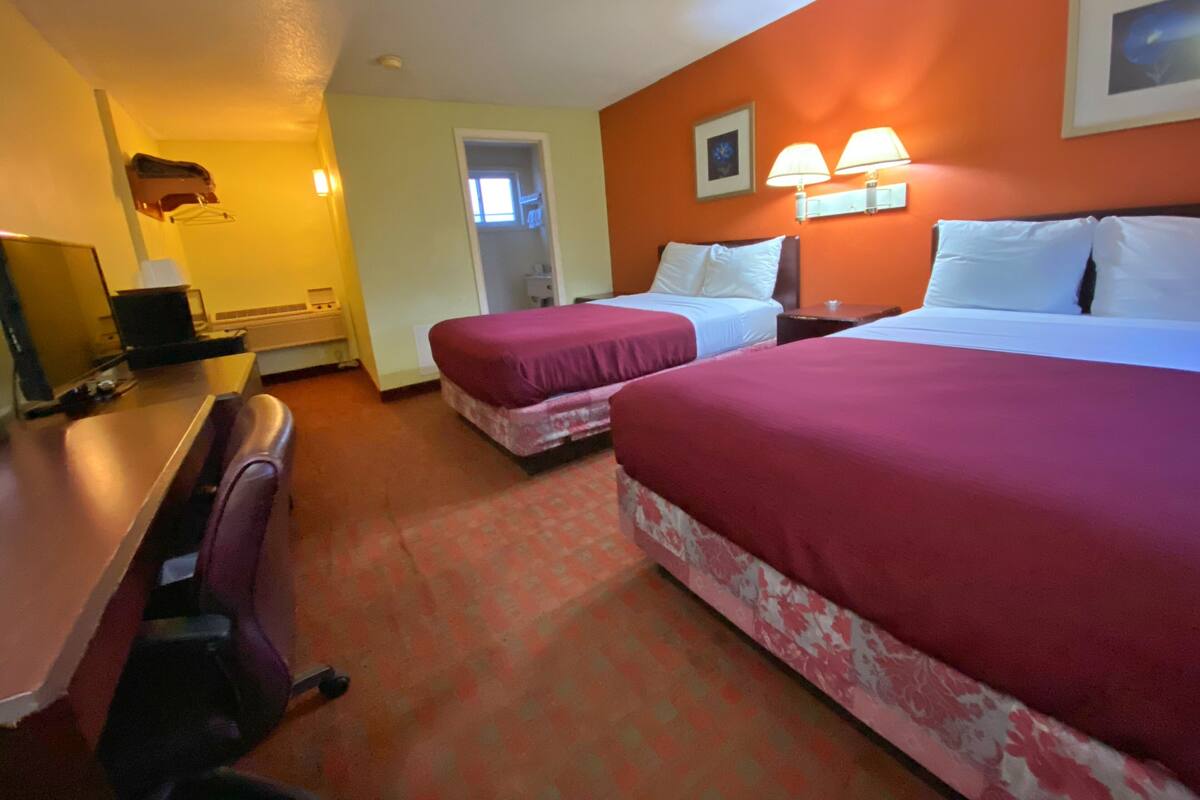 A hotel room with two beds, a desk, a chair, and a small table.