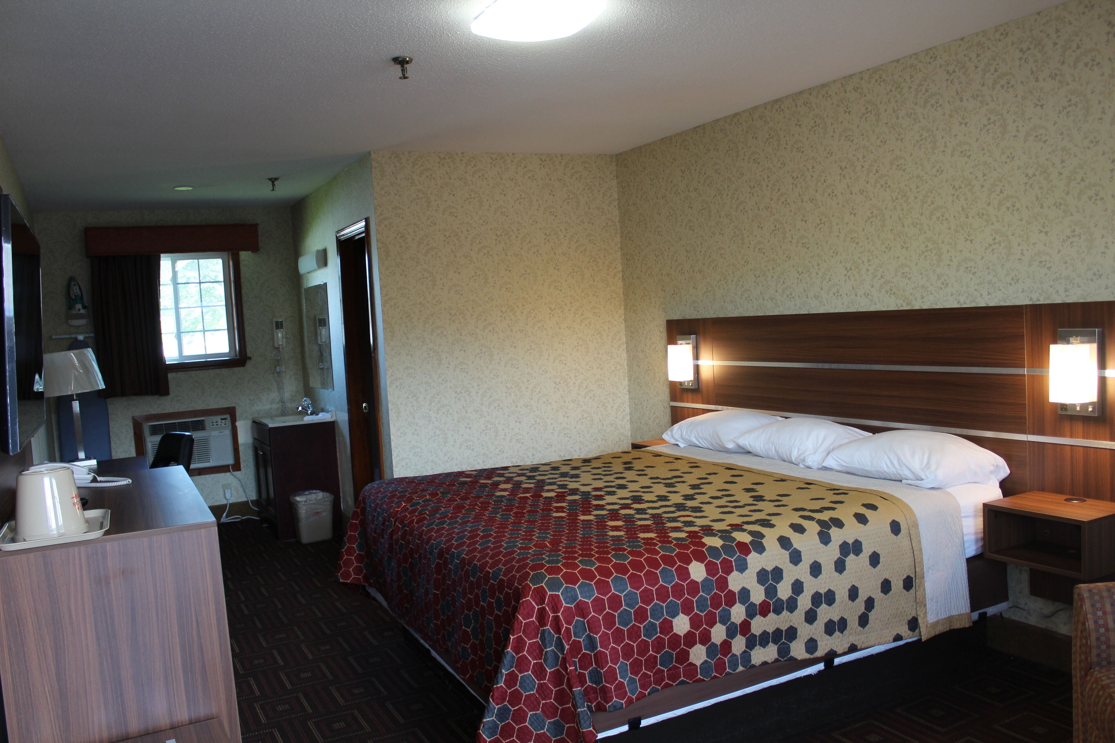 A hotel room with a bed, bedside table, lamp, and a desk with a chair.