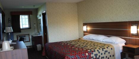 A hotel room with a bed, bedside table, lamp, and a desk with a chair.