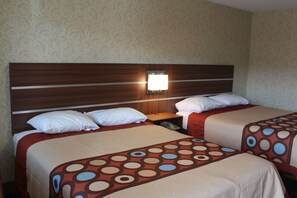 A hotel room with two beds, each with a patterned bedspread, a wooden headboard, and a bedside lamp.