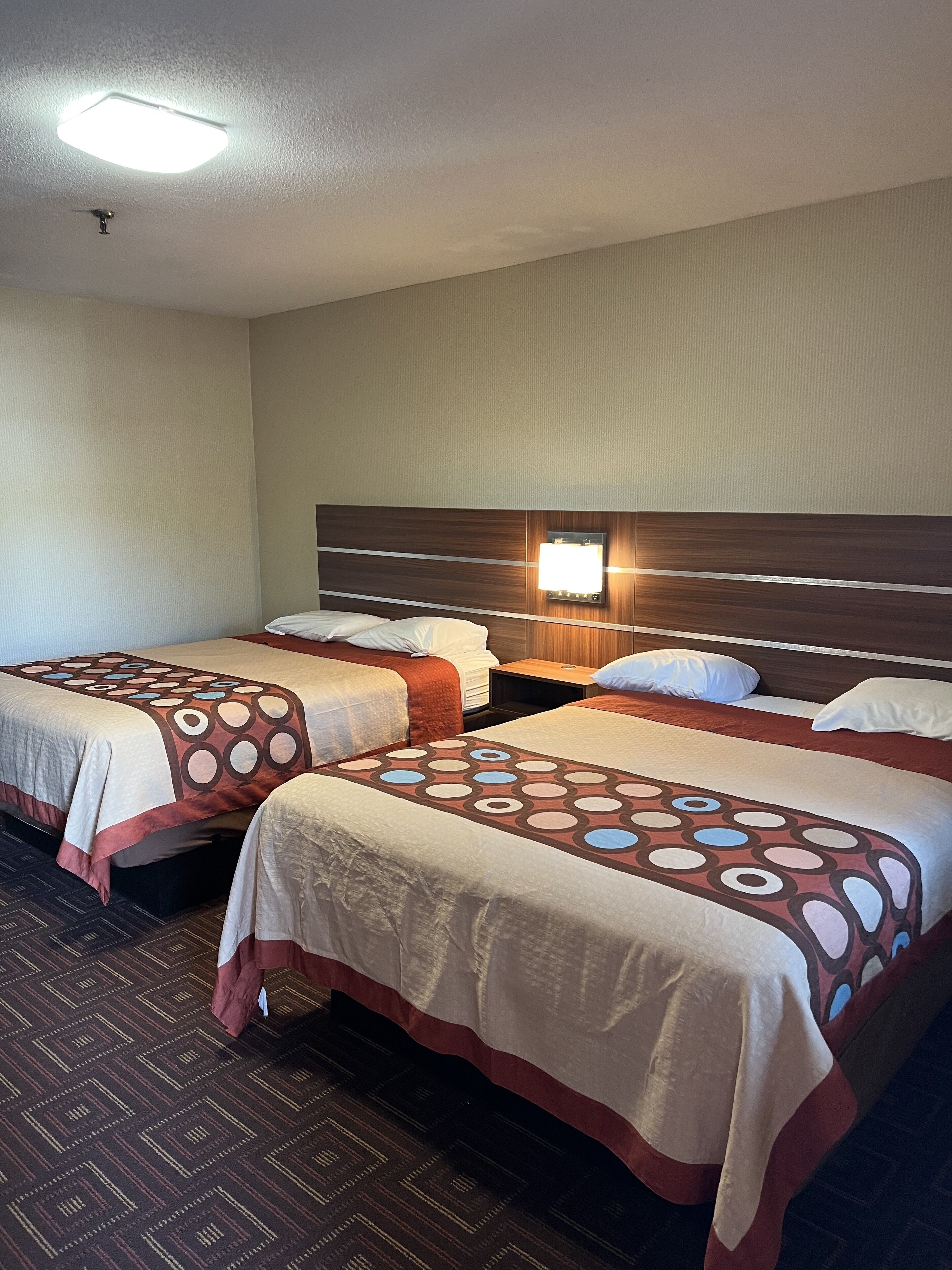 Habitación de hotel con dos camas, cabecera con lámpara y alfombra estampada.