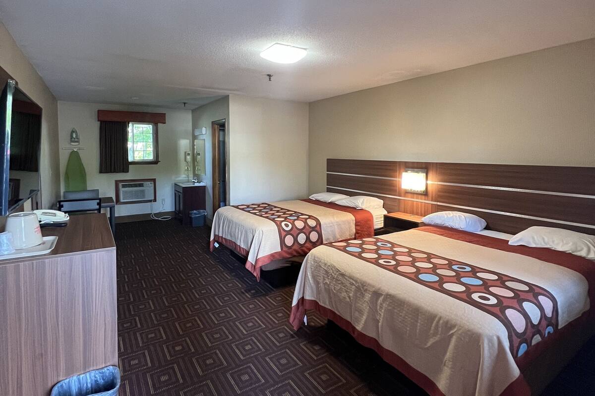 Habitación de hotel con tres camas, un escritorio, un espejo y una ventana.