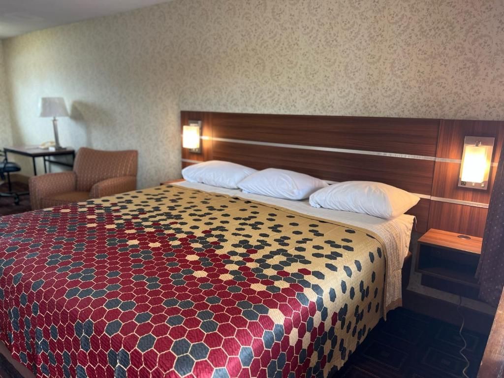 A hotel room with a bed, a nightstand, a lamp, and a chair.
