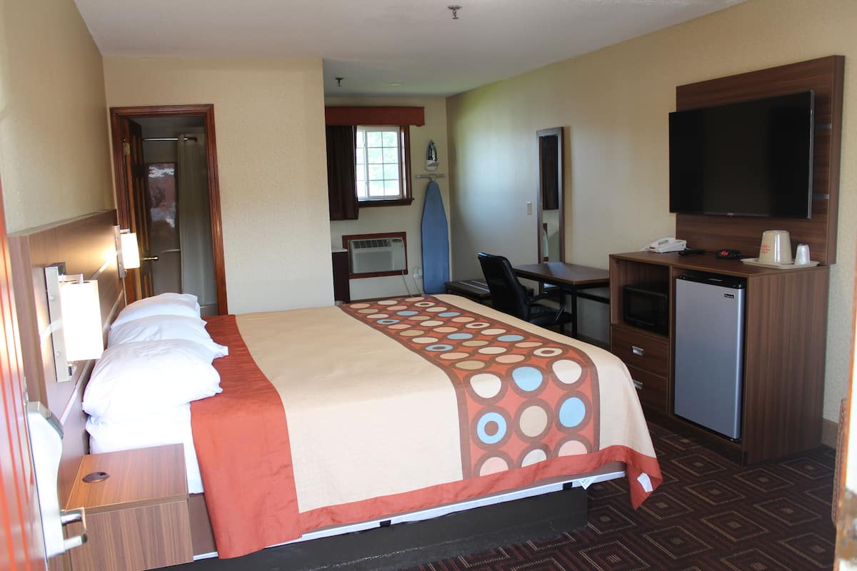 Una habitación de hotel con cama, escritorio, televisor y kitchenette.