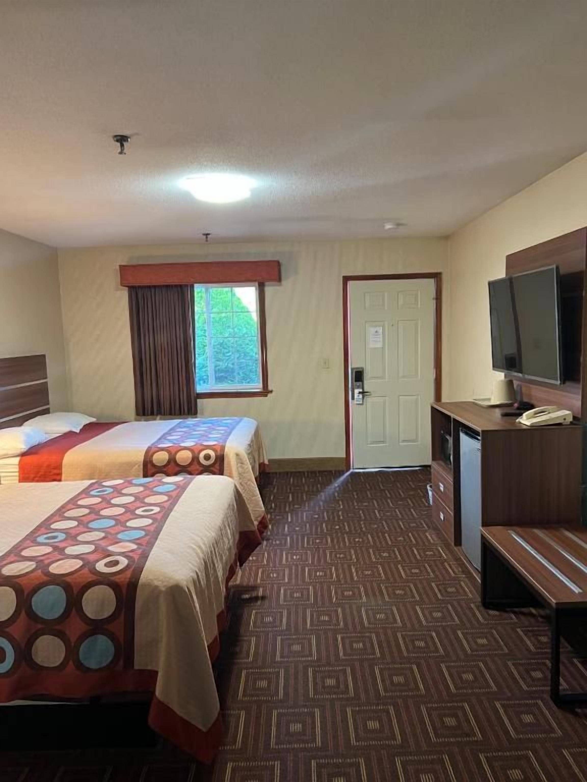 Habitación de hotel con dos camas, un escritorio, un televisor y una puerta.