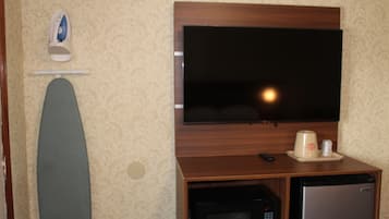 A room with a flat-screen TV mounted on a wooden cabinet, a microwave, a refrigerator, and an ironing board.