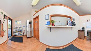 A reception area with a counter, a refrigerator, a small cabinet, a chair, and a window with a view of the street. - American Inn (Branford)