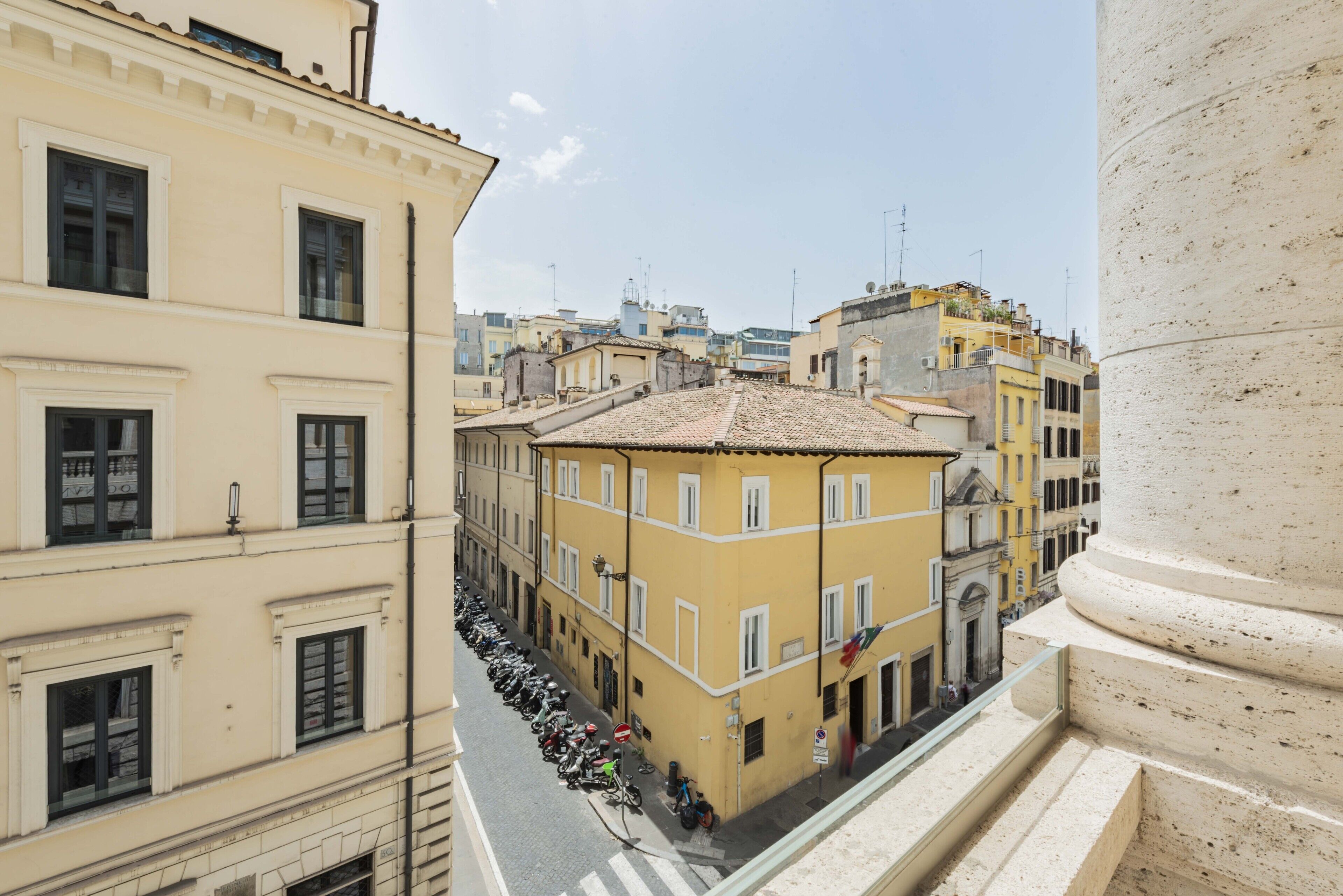 A street view with buildings, a row of parked motorcycles, and a clear sky.