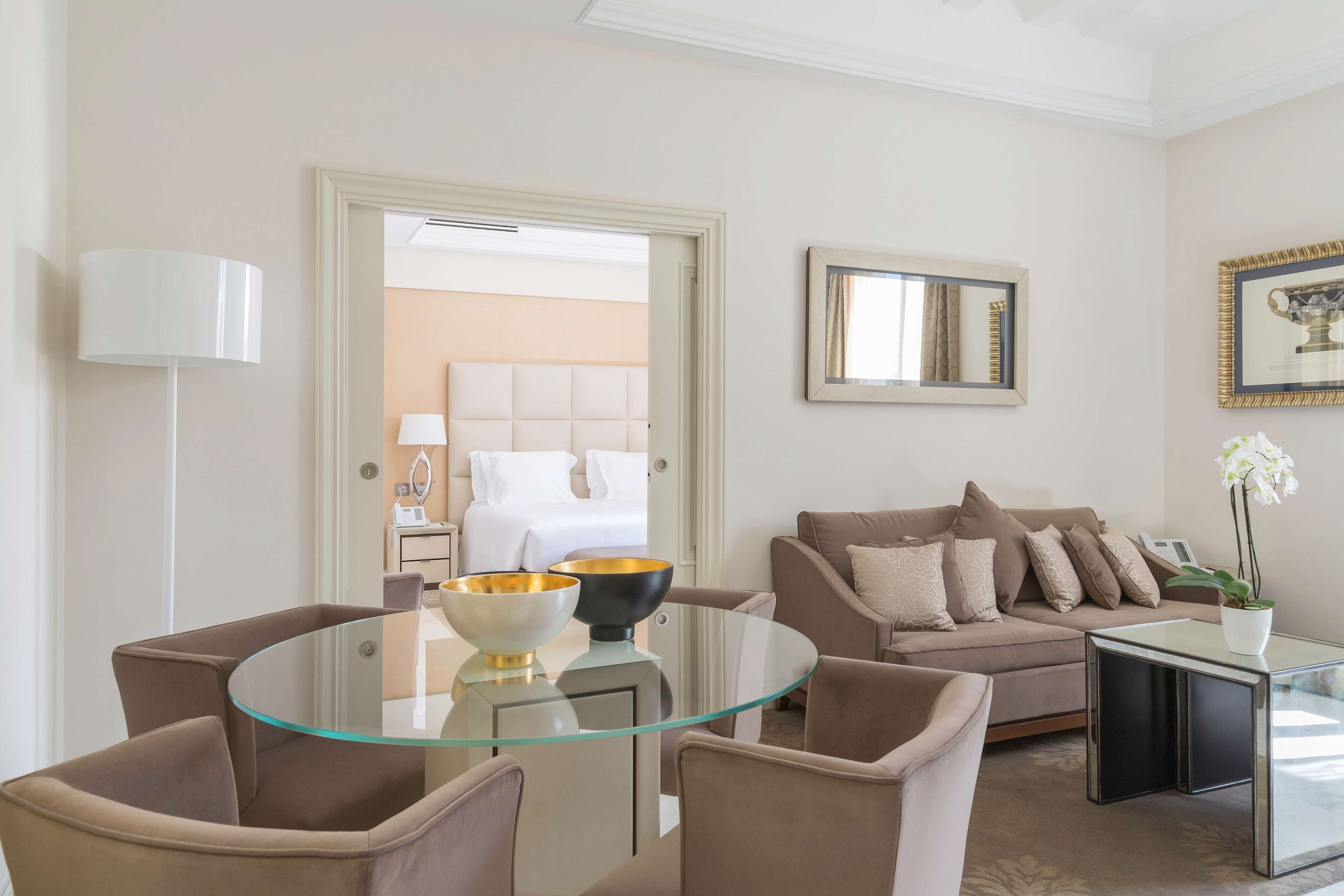 A modern living room with a glass coffee table, beige sofas, and a dining area with a glass table and chairs.