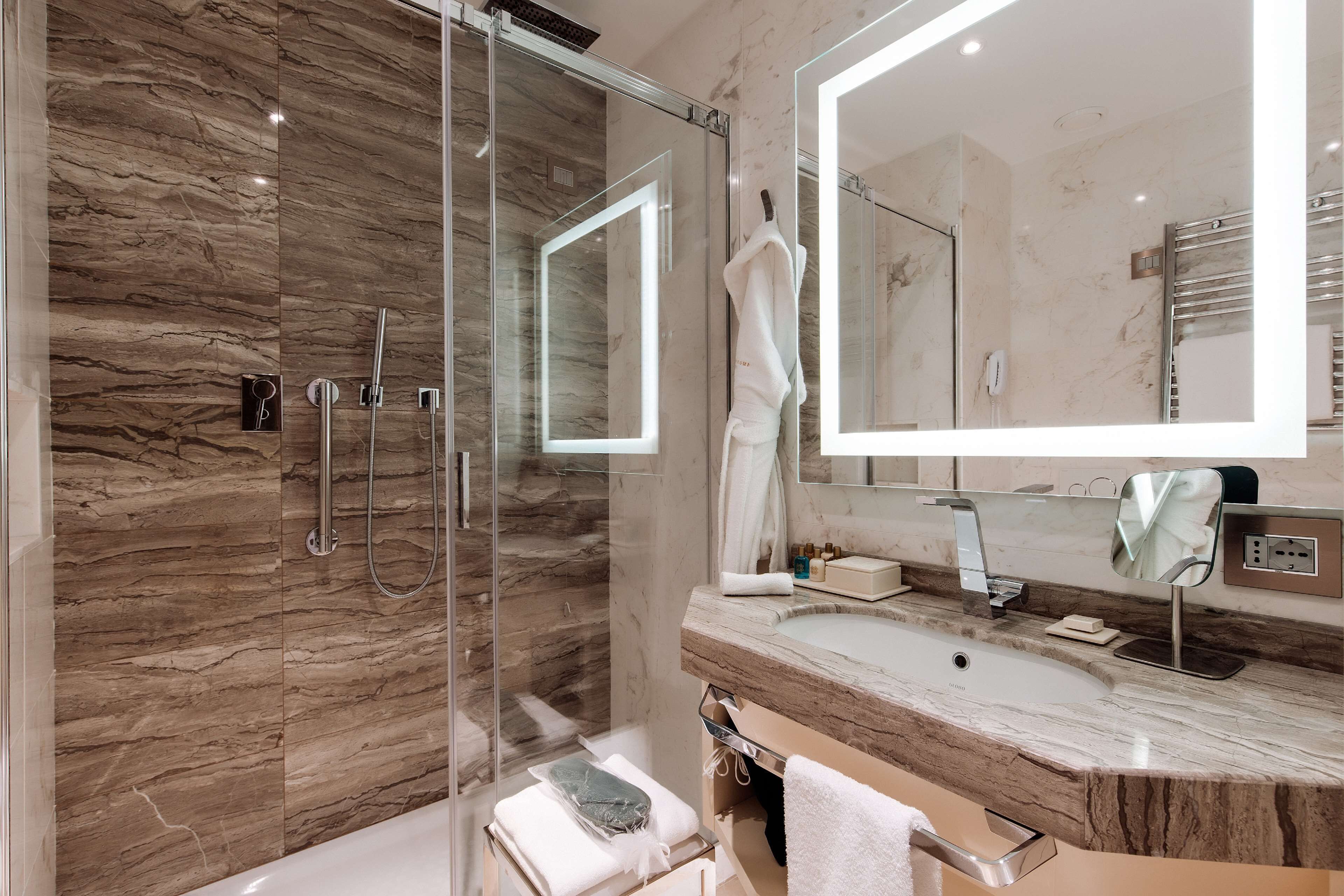 Un baño moderno con cabina de ducha de vidrio, un espejo grande y encimera de mármol.