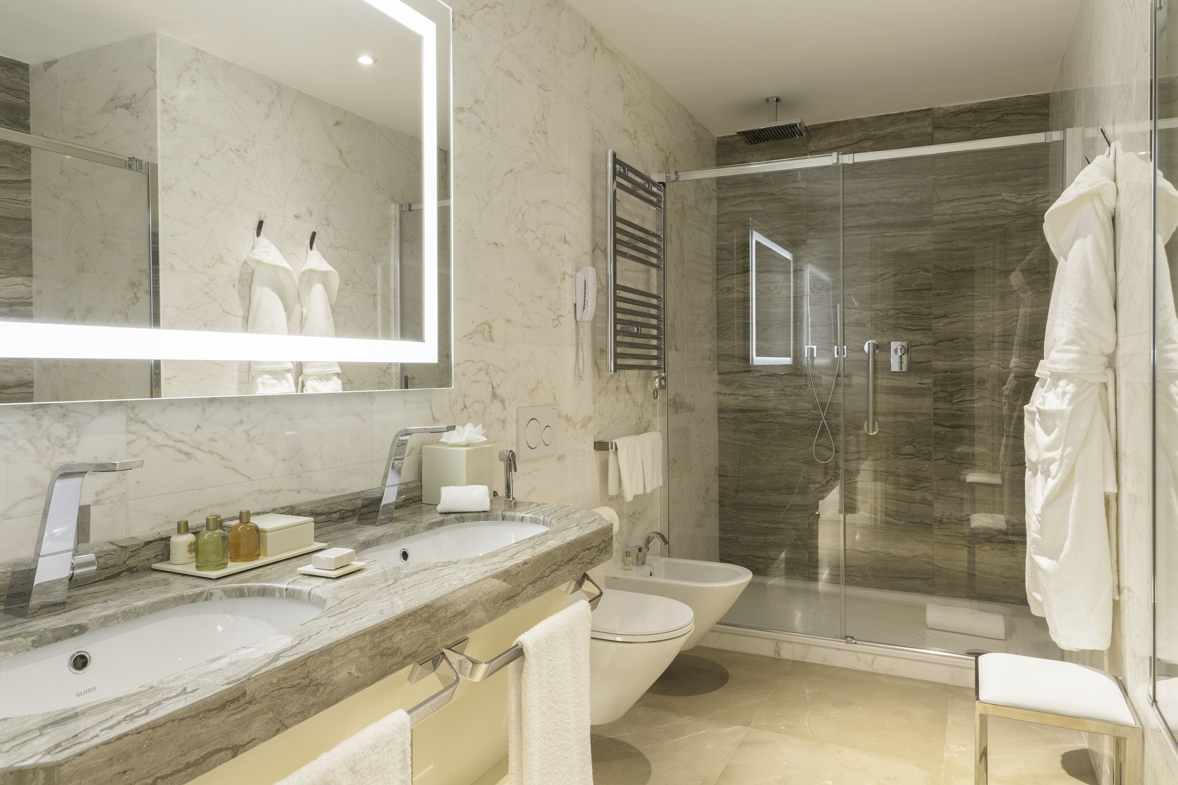Une salle de bain moderne avec un meuble-lavabo en marbre, une cabine de douche en verre et des toilettes séparées.