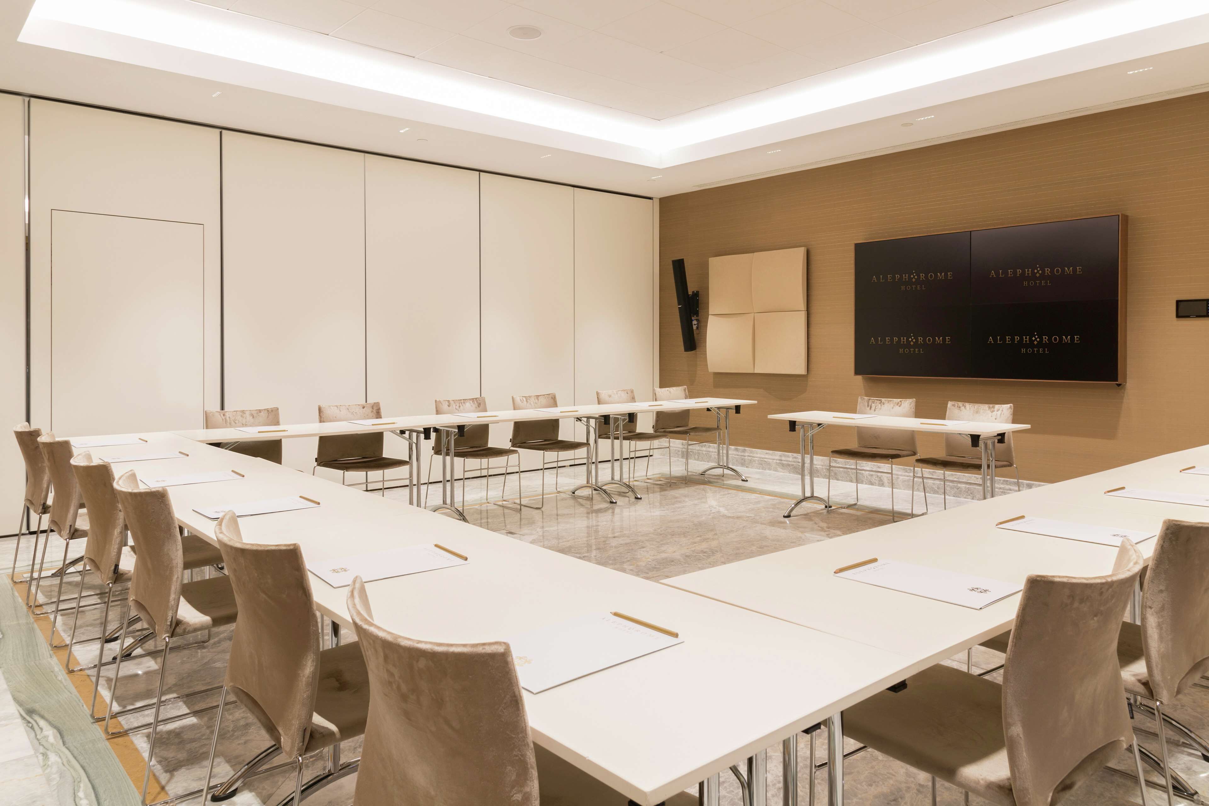 A conference room with long tables and chairs, a large screen displaying hotel information, and a modern interior design.