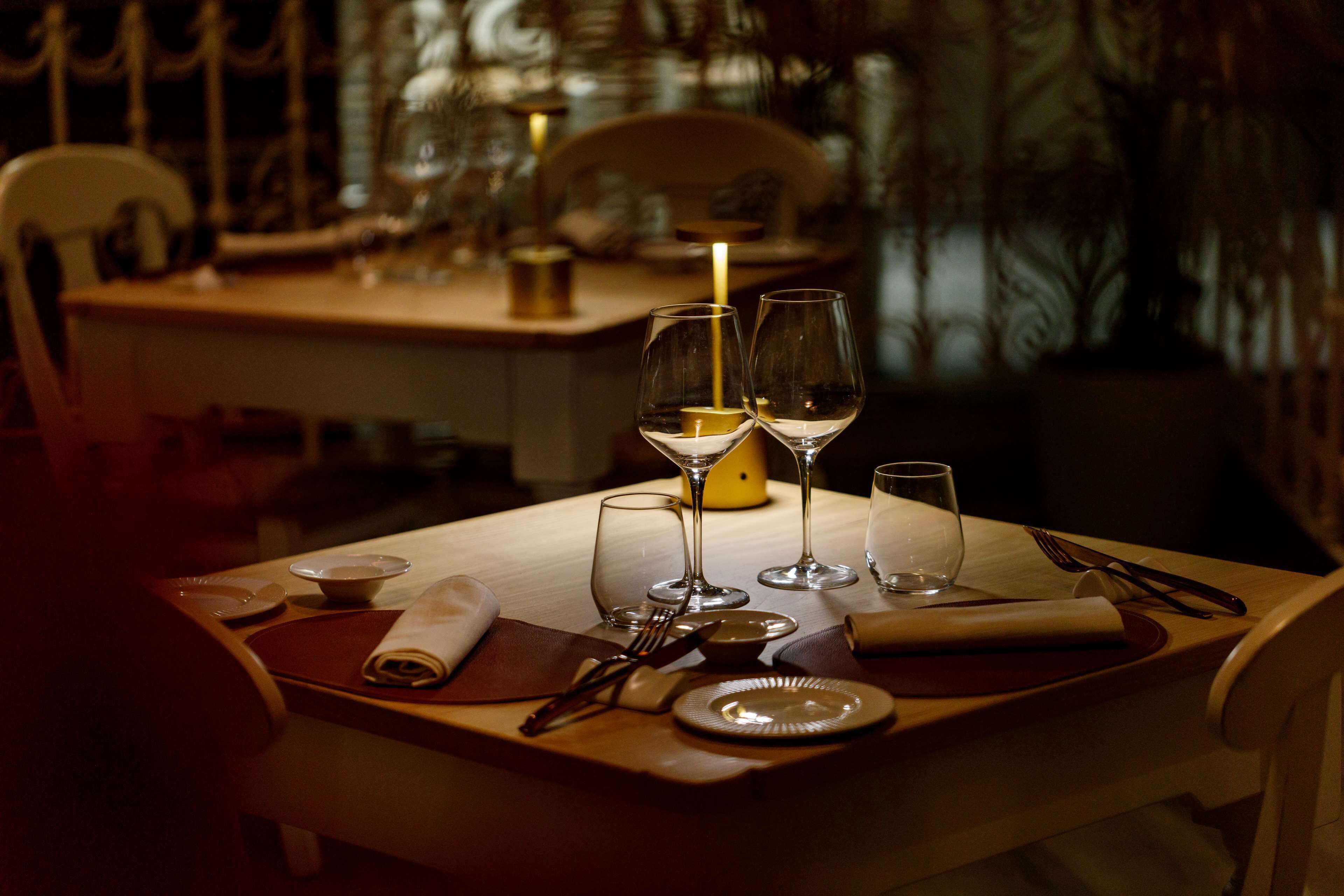 Una mesa de comedor dispuesta con platos, cubiertos y copas de vino, con una vela sobre la mesa.