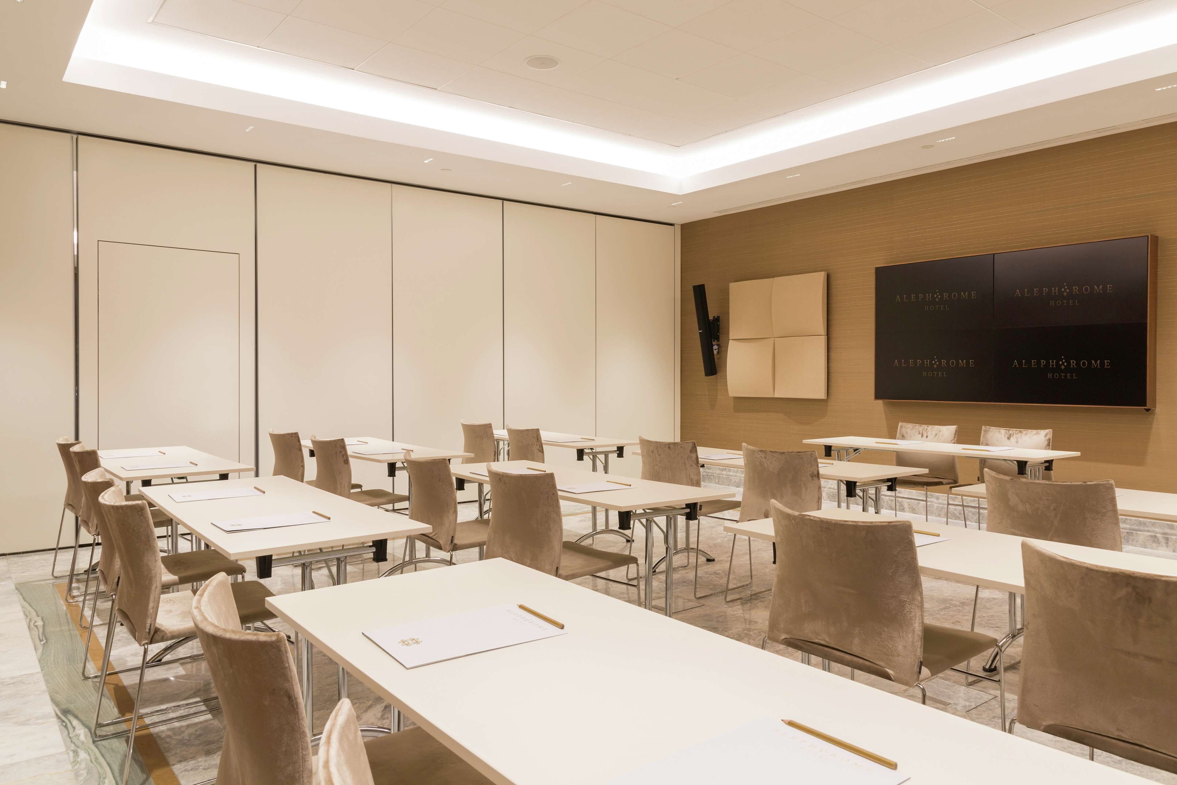 Ein moderner Konferenzraum mit beigen Stühlen und Tischen, einer Wand als Holzdekor und einer Decke mit eingelassener Beleuchtung.