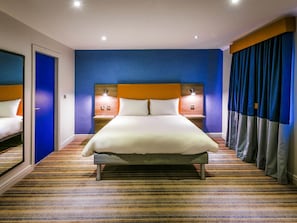 A hotel room with a large bed, two bedside tables with lamps, a blue door, and a striped carpet.