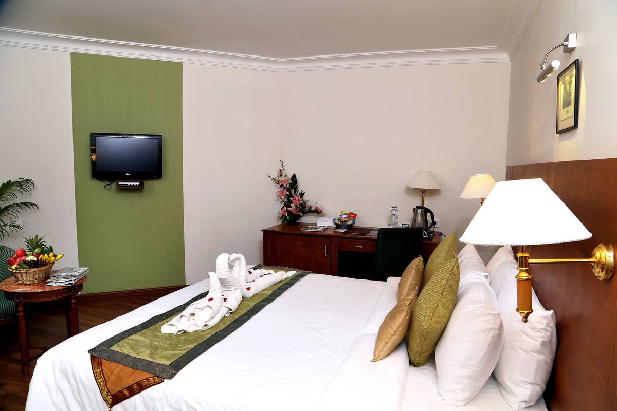 Ein Hotelzimmer mit einem Bett, einem Schreibtisch mit Lampe, einem Fernseher und einer grünen Wand.