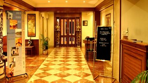 Um hall de hotel com piso de mármore quadriculado, painéis de madeira e um balcão de recepção.