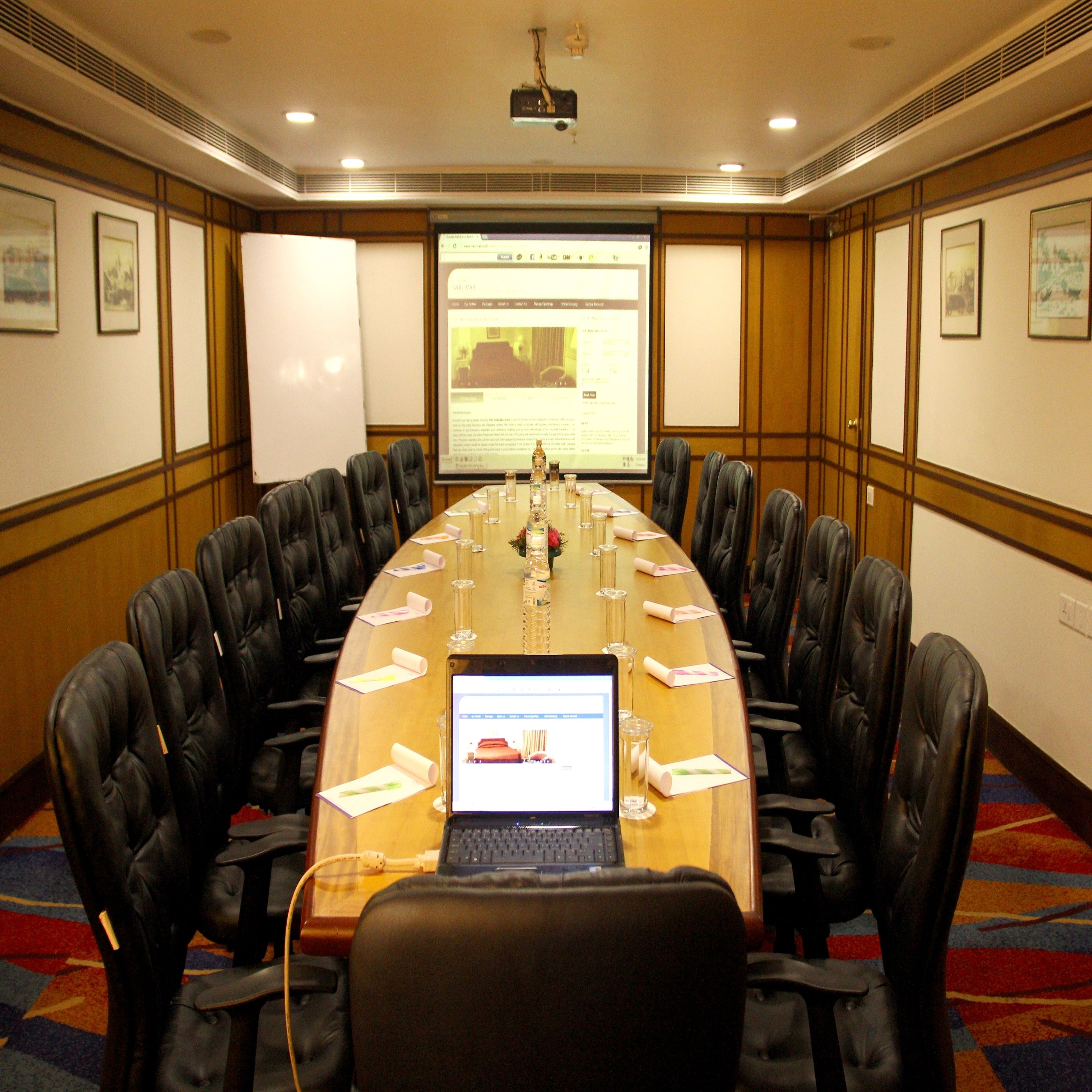 A conference room with a long table, black leather chairs, a laptop, and a projector screen displaying a webpage.