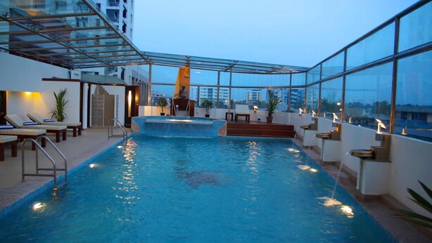 Piscina no terraço com paredes de vidro transparente, espreguiçadeiras e uma cascata.