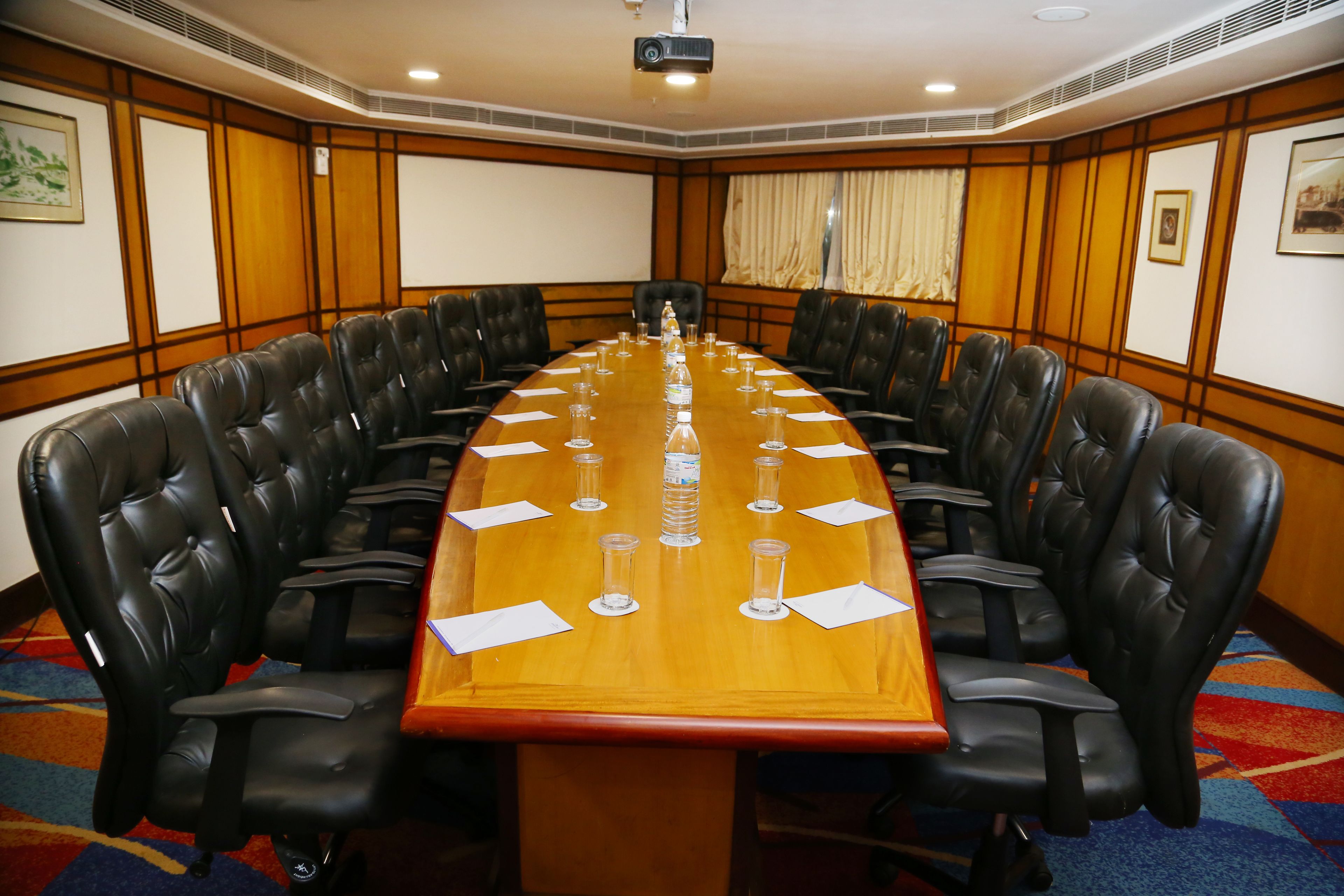 A conference room with a long table, black leather chairs, and a projector screen.