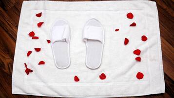 Une serviette blanche, une paire de chaussons blancs et des pétales de roses rouges éparpillés sur un plancher en bois.