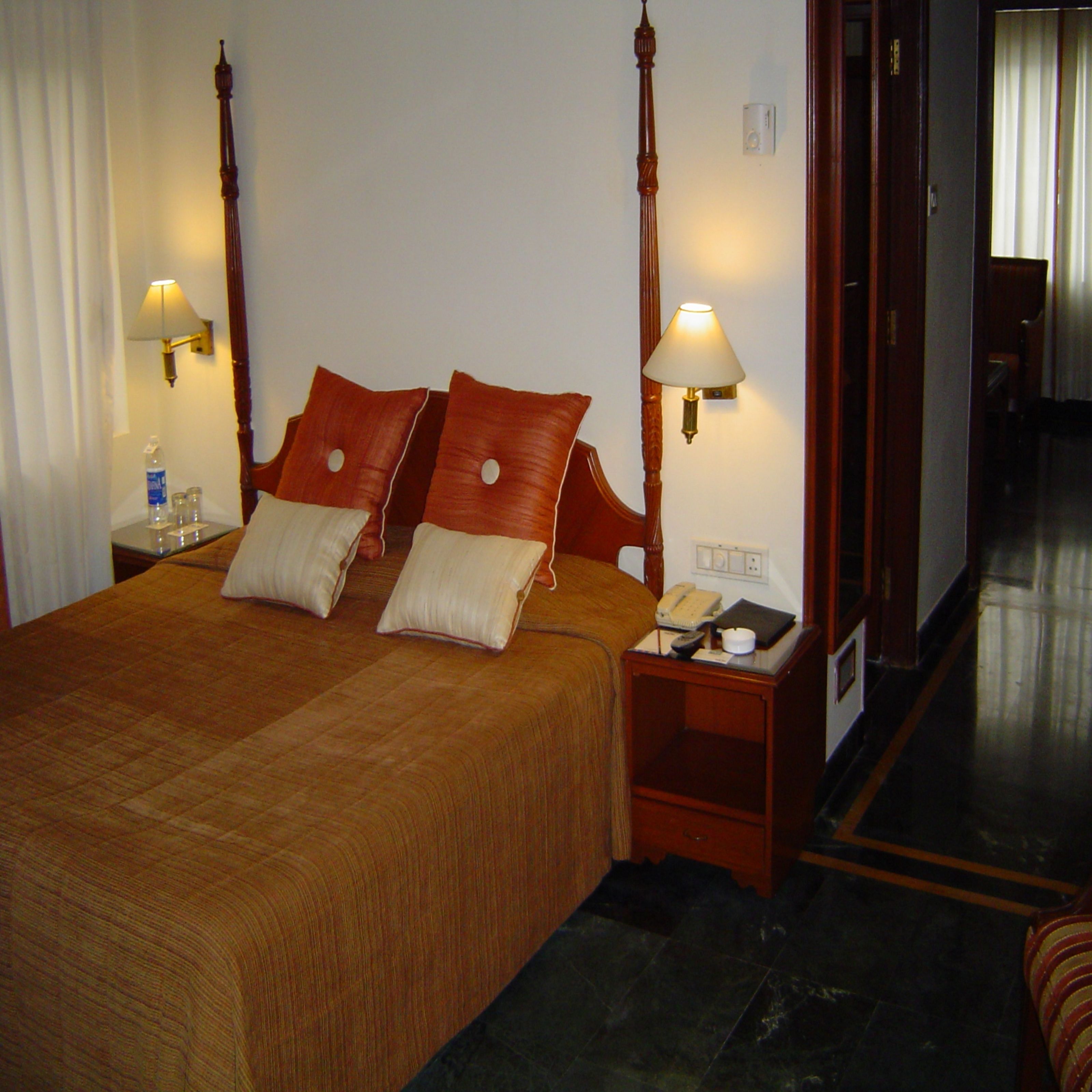 Habitación de hotel con cama con dosel, dos lámparas de noche, una mesita de noche con teléfono y una botella de agua sobre la mesita.