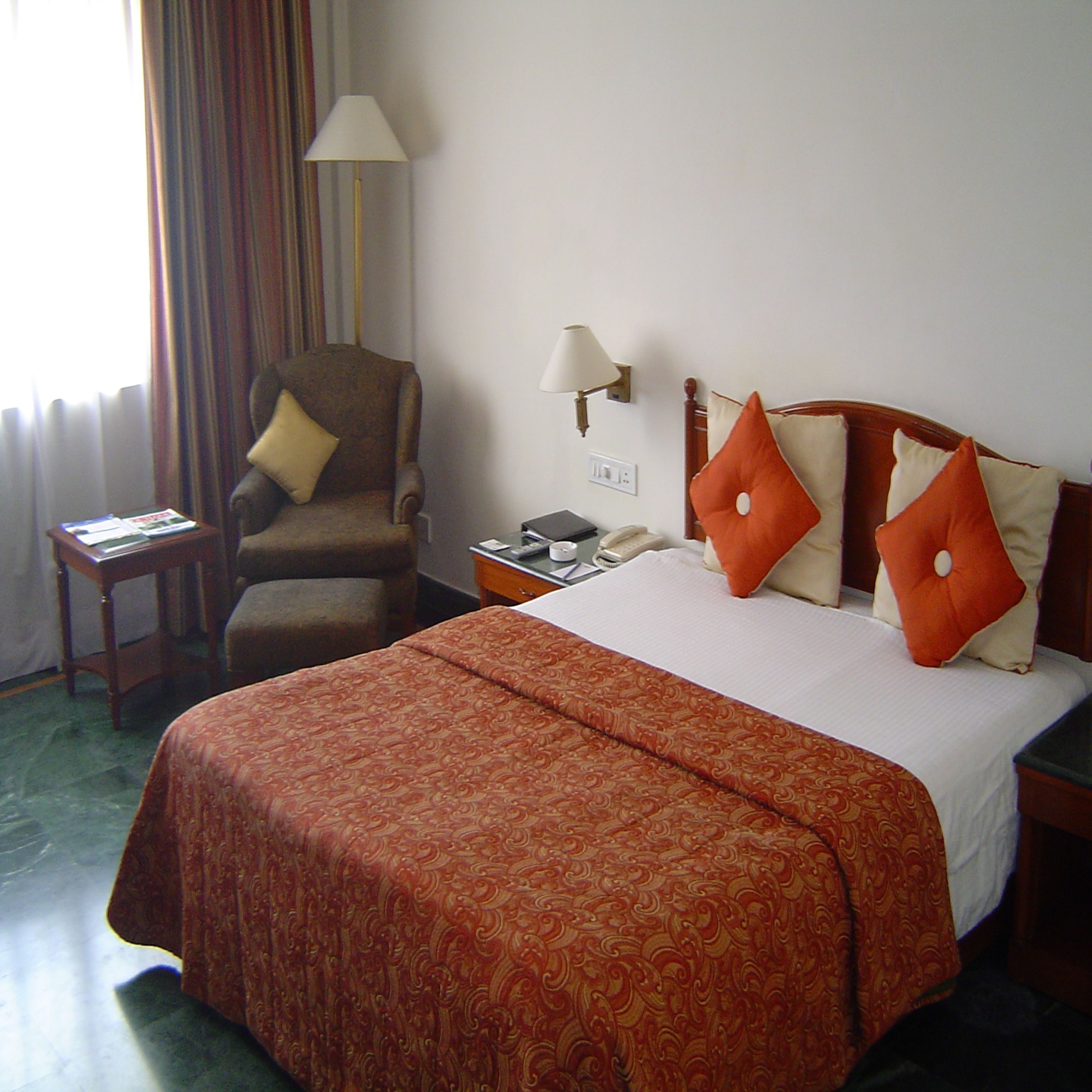 A hotel room with a large bed, a chair, a nightstand, and a lamp.
