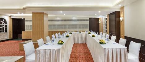 A conference room with a long table, white chairs, and a red carpeted floor.