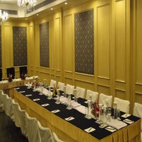 Un salón de conferencias con una larga mesa dispuesta para una reunión, rodeado de sillas, con papel tapiz estampado y una araña de cristal.