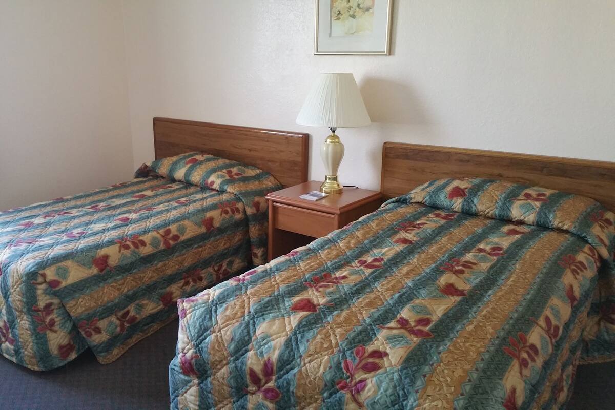 A hotel room with two single beds, a nightstand with a lamp, and a framed picture on the wall.