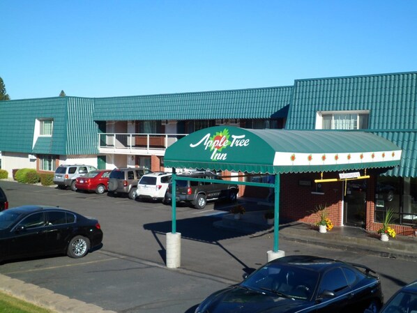 A hotel named Apple Tree Inn with a green awning, a parking lot with several cars, and a brick building facade.
