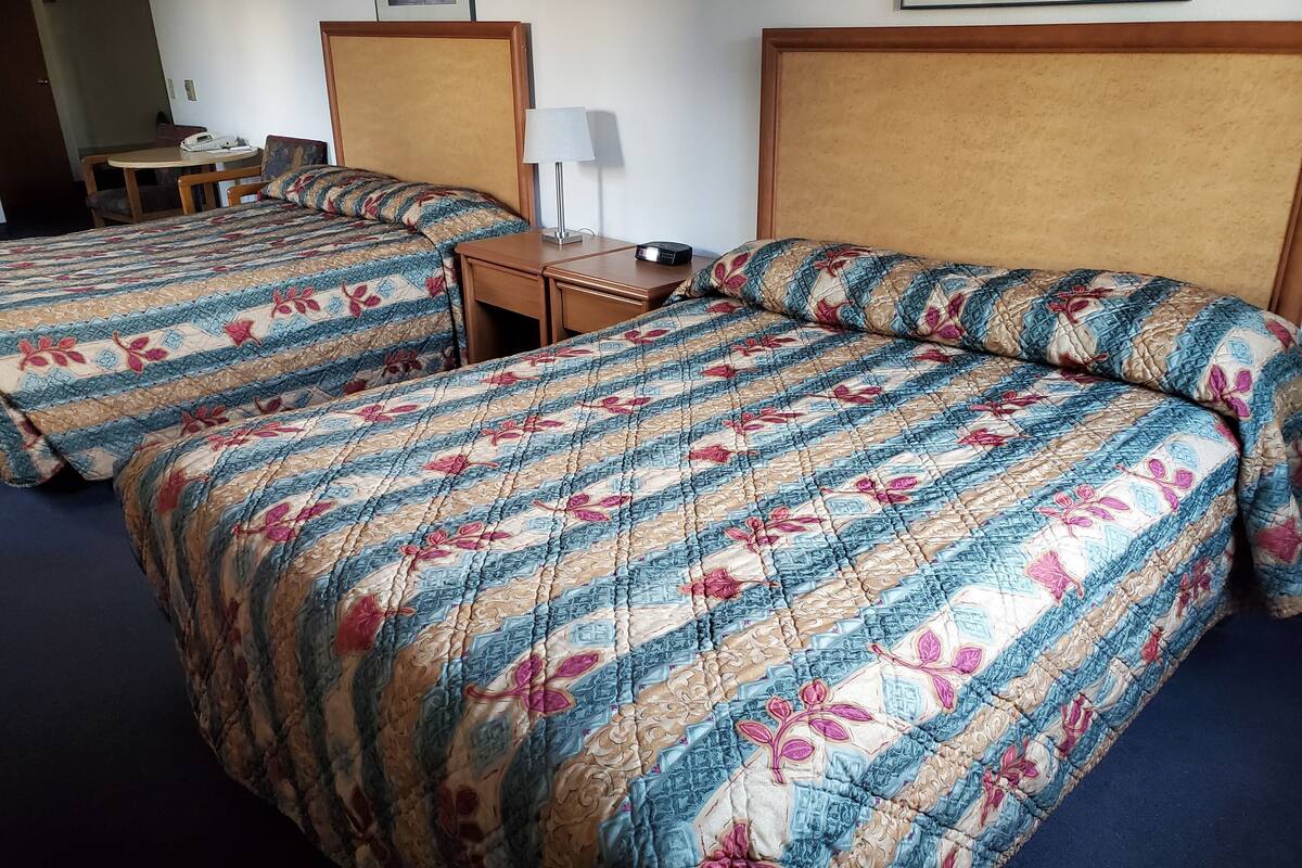 A hotel room with two beds, each with a floral-patterned bedspread, a bedside table with a lamp, and a small table with a telephone.