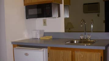 A compact kitchen with wooden cabinets, a built-in microwave, a sink with a faucet, and a small refrigerator.