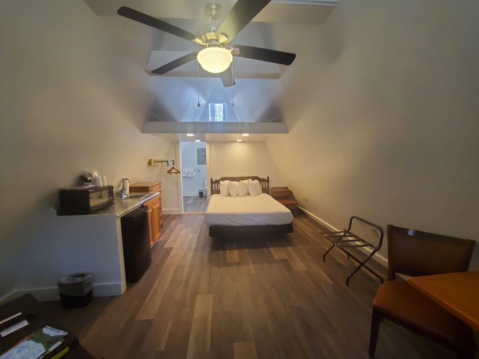 A compact room with a bed, a desk, a chair, and a ceiling fan.