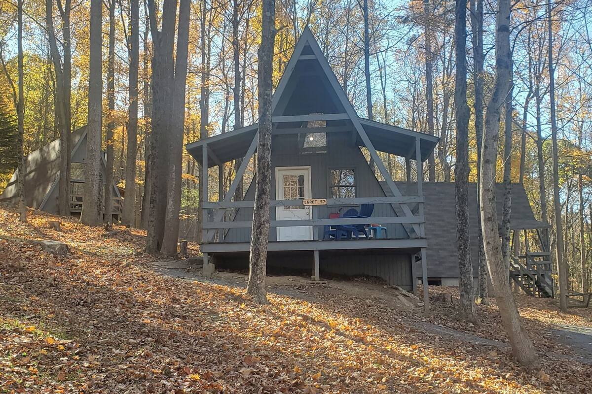 A cabin with a triangular roof, a porch with chairs, and a sign reading "EGRET 57".
