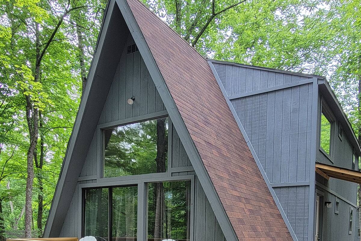 A cabin with a sloped roof, large windows, and a wooden deck with chairs.