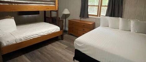 A room with two bunk beds, a wooden dresser, a lamp, and a window with curtains.
