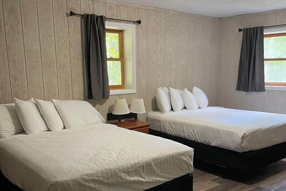 A room with two beds, wooden flooring, and a window with curtains.