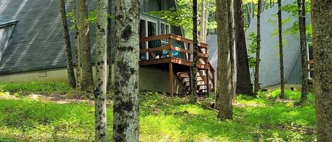 Una cabaña con terraza de madera, rodeada de árboles y un área verde.