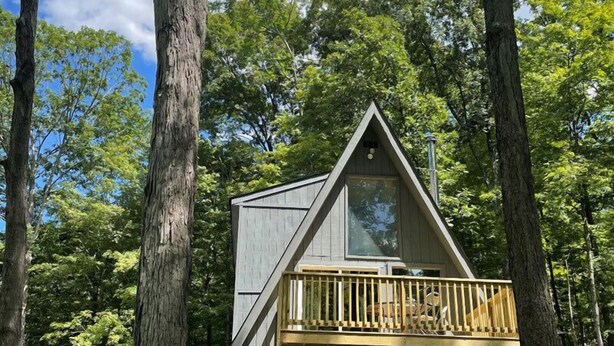 A cabin with a wooden deck and a triangular roof, surrounded by trees. - Coolfont Resort (Berkeley Springs)