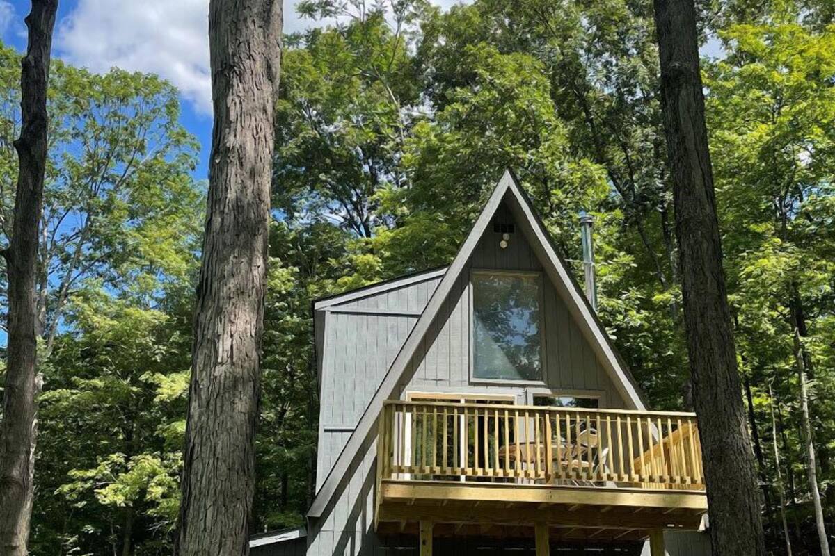 A cabin with a wooden deck and a triangular roof, surrounded by trees.