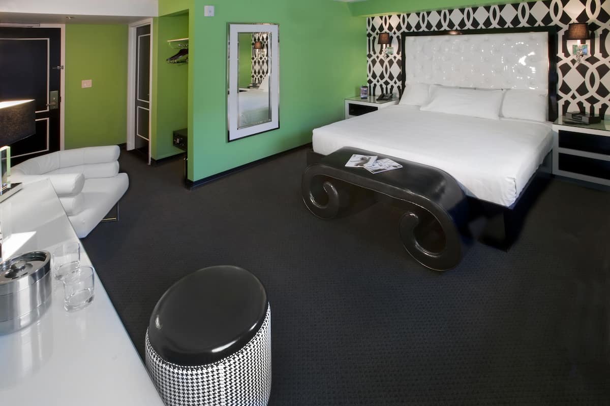 A modern hotel room with a bed, a desk, a chair, and a trash bin.