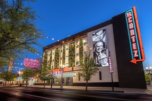 A hotel with a neon sign, a large mural, and a street view.