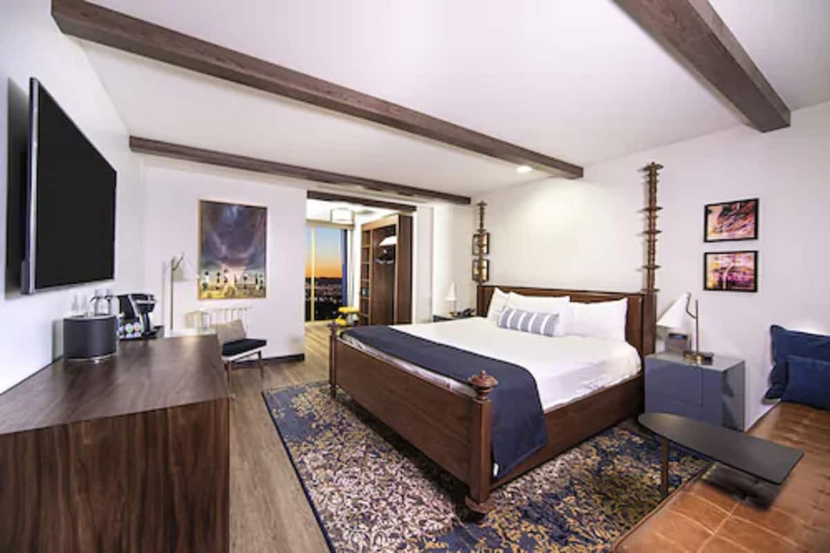 A hotel room with a large bed, a desk, a TV, and a view of the city.