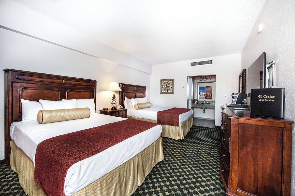 A hotel room with two beds, a desk, a mirror, and a television.