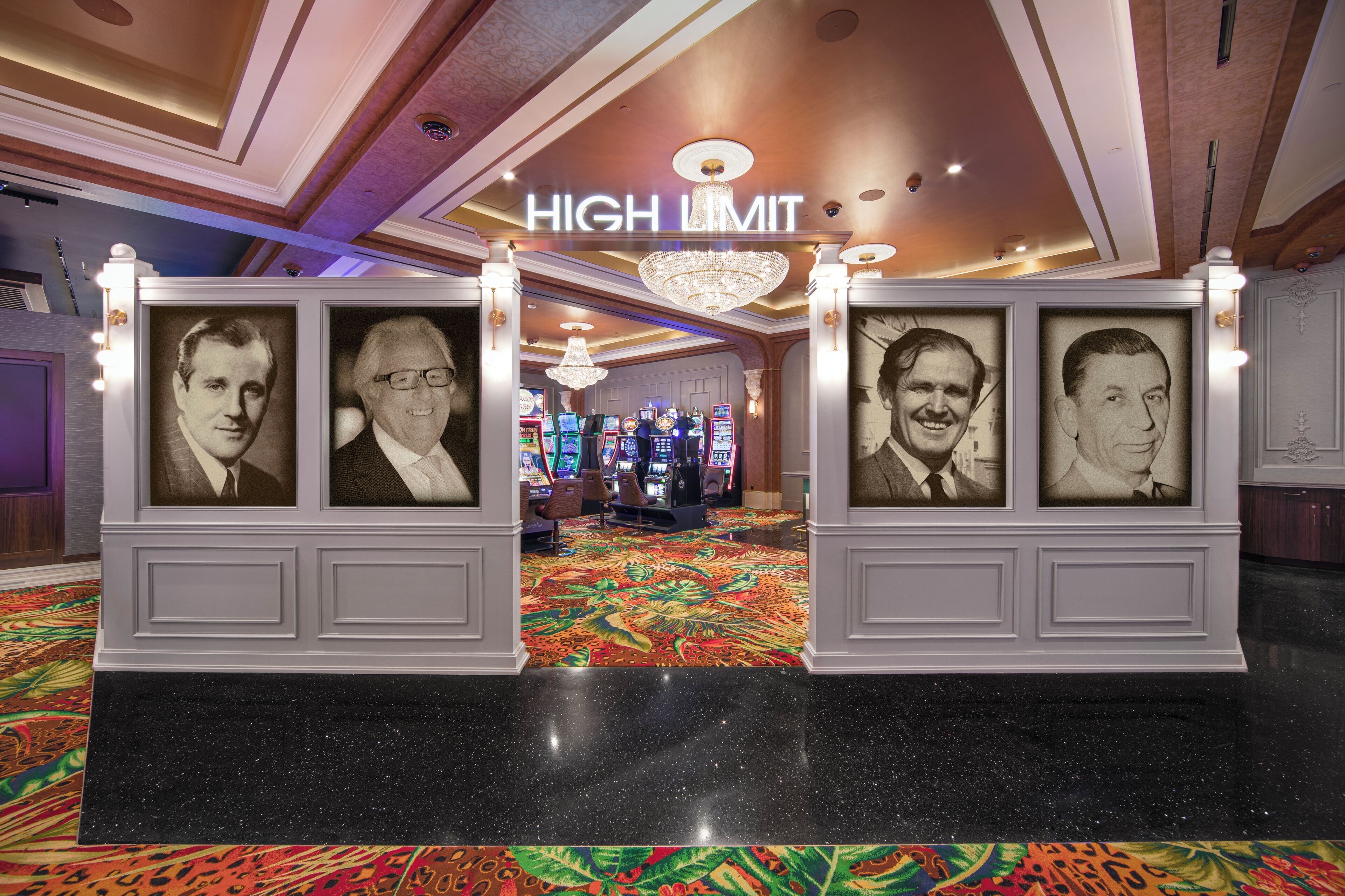 A lobby with a 'HIGH LIMIT' sign, framed portraits, a chandelier, and a carpeted floor.