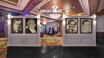 A lobby with a 'HIGH LIMIT' sign, framed portraits, a chandelier, and a carpeted floor.