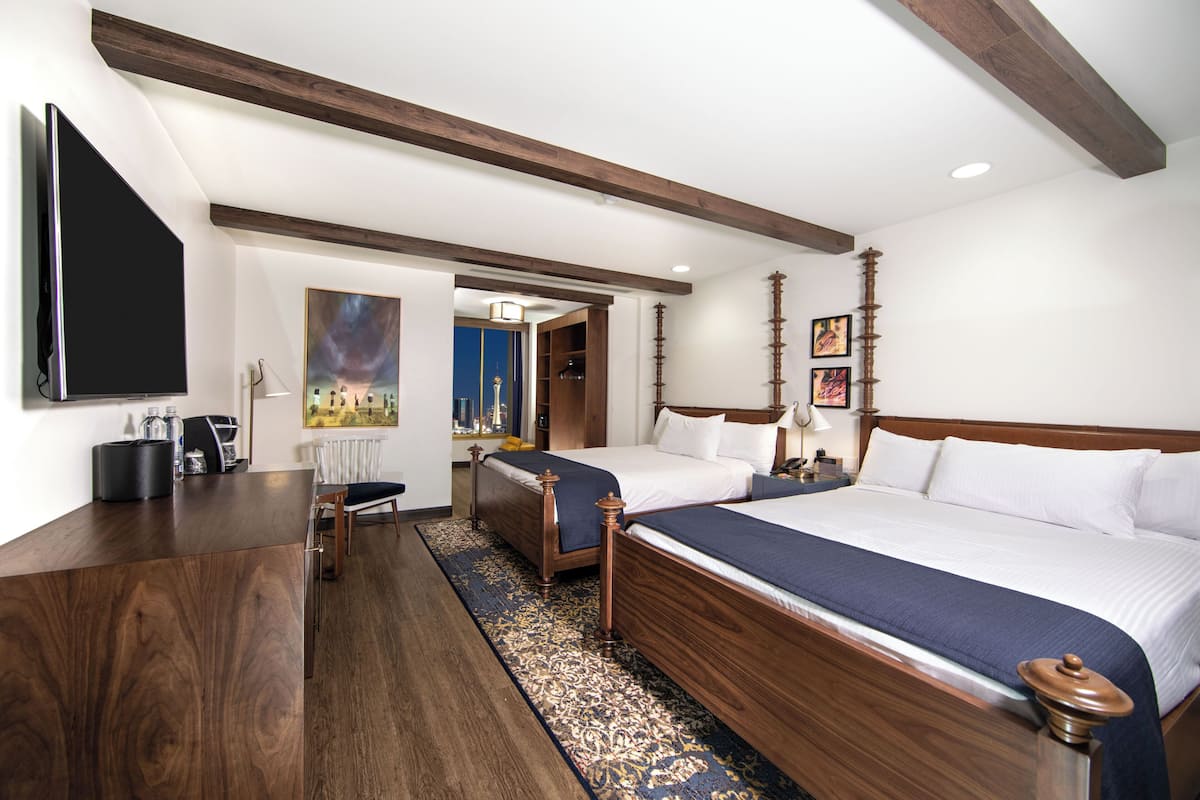 A hotel room with a large bed, a desk, a chair, a TV, and a painting on the wall.