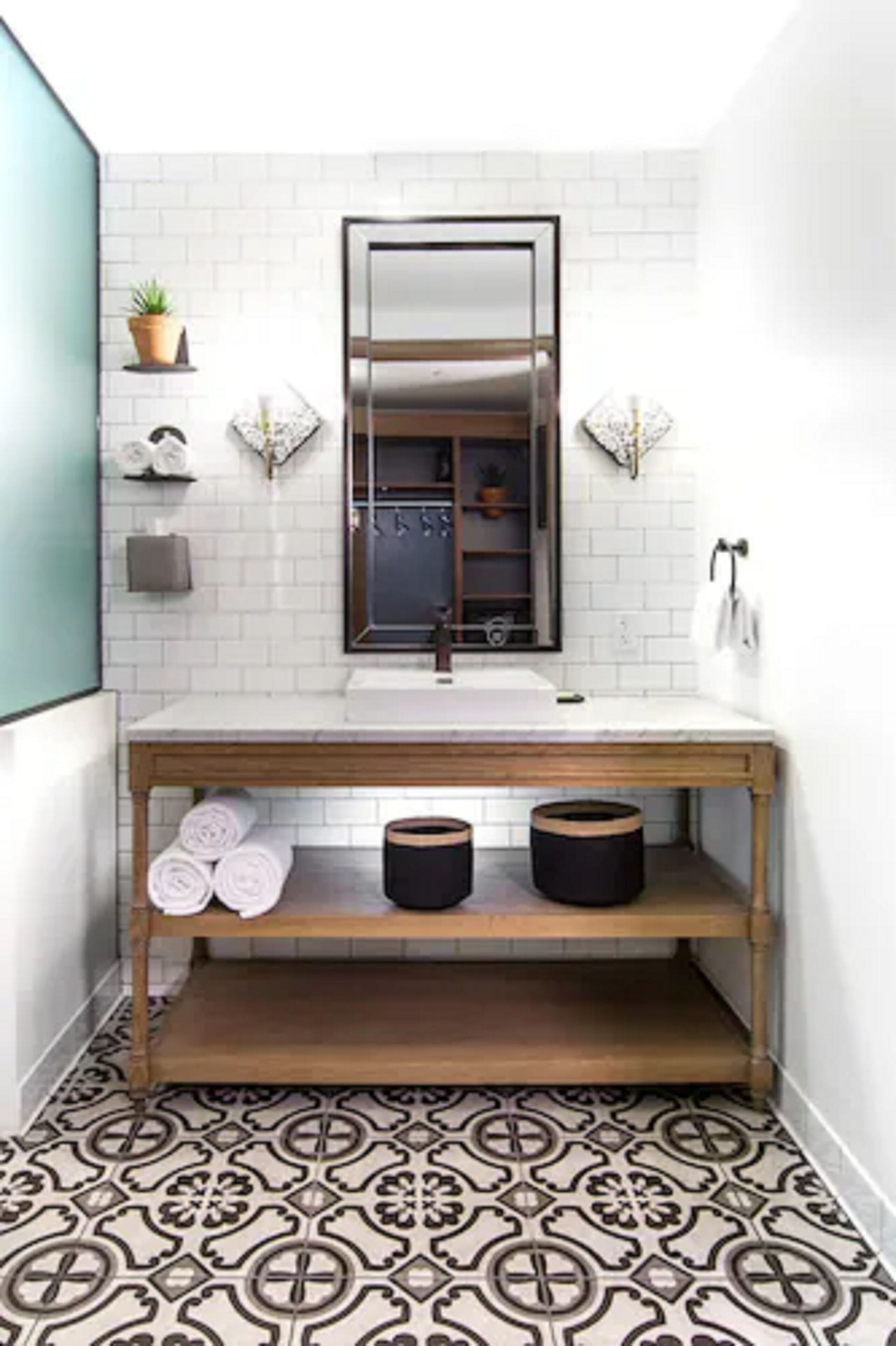 Un baño con salpicadero de azulejos blancos, tocador de madera, espejo y suelo estampado.